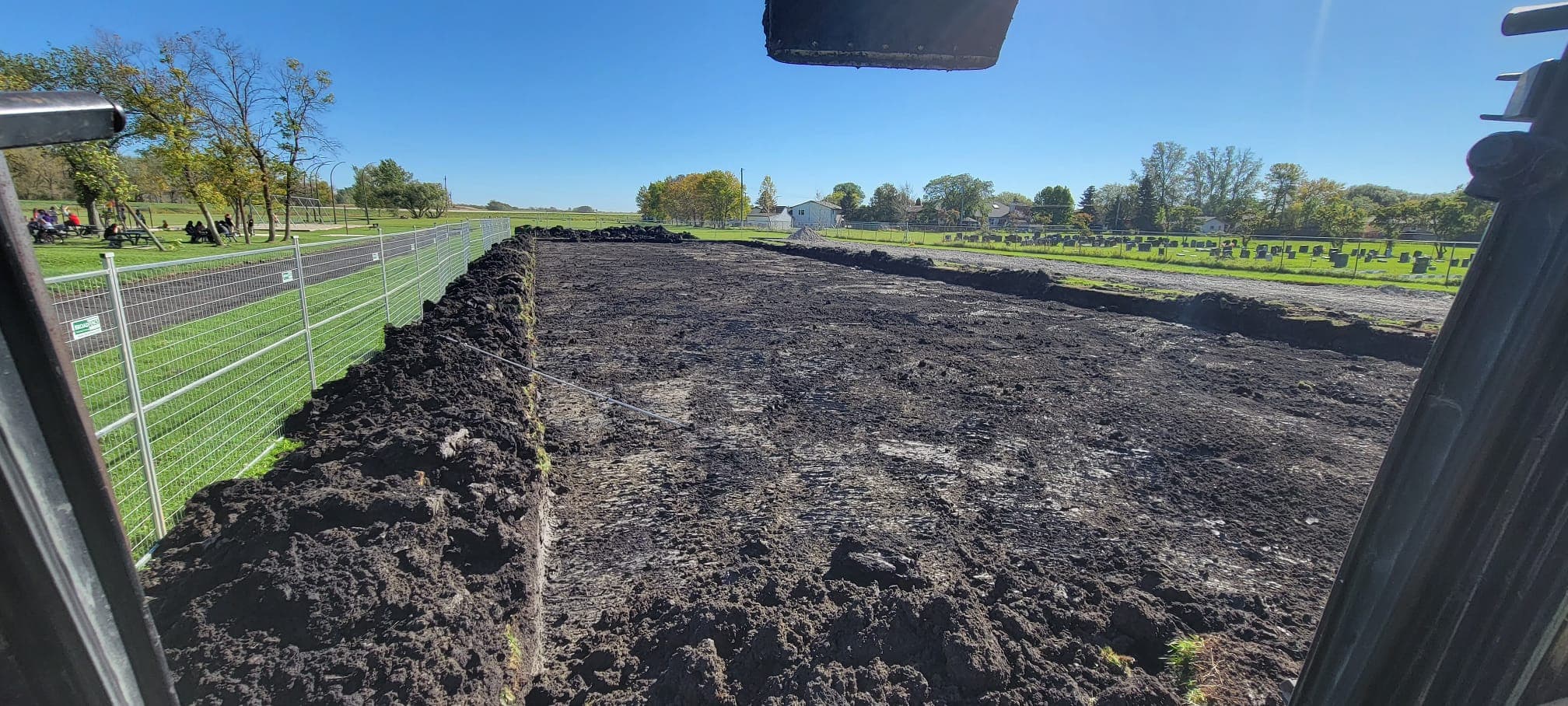 Large rectangular plot of dark soil at a construction site, viewed from inside heavy machinery.