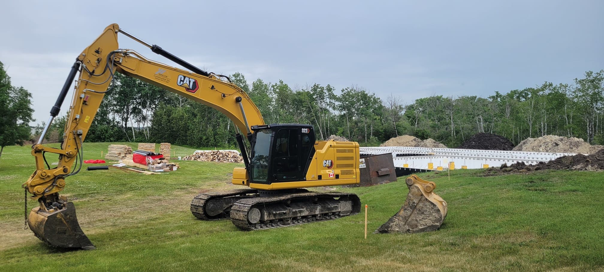 Yellow CAT excavator parked on grass at a construction site with a building foundation.
