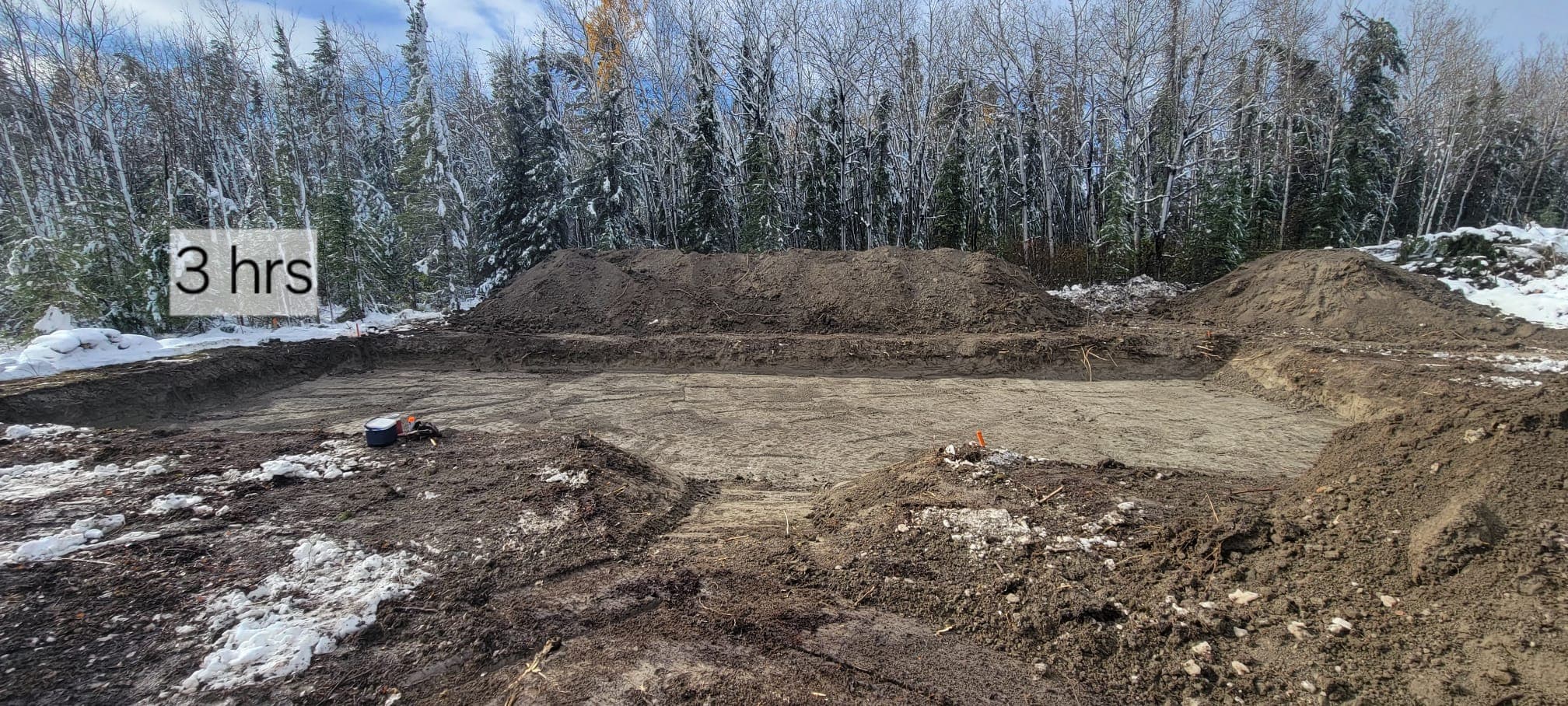 Excavated rectangular pit with dirt mounds in a snowy forest, labeled "3 hrs".