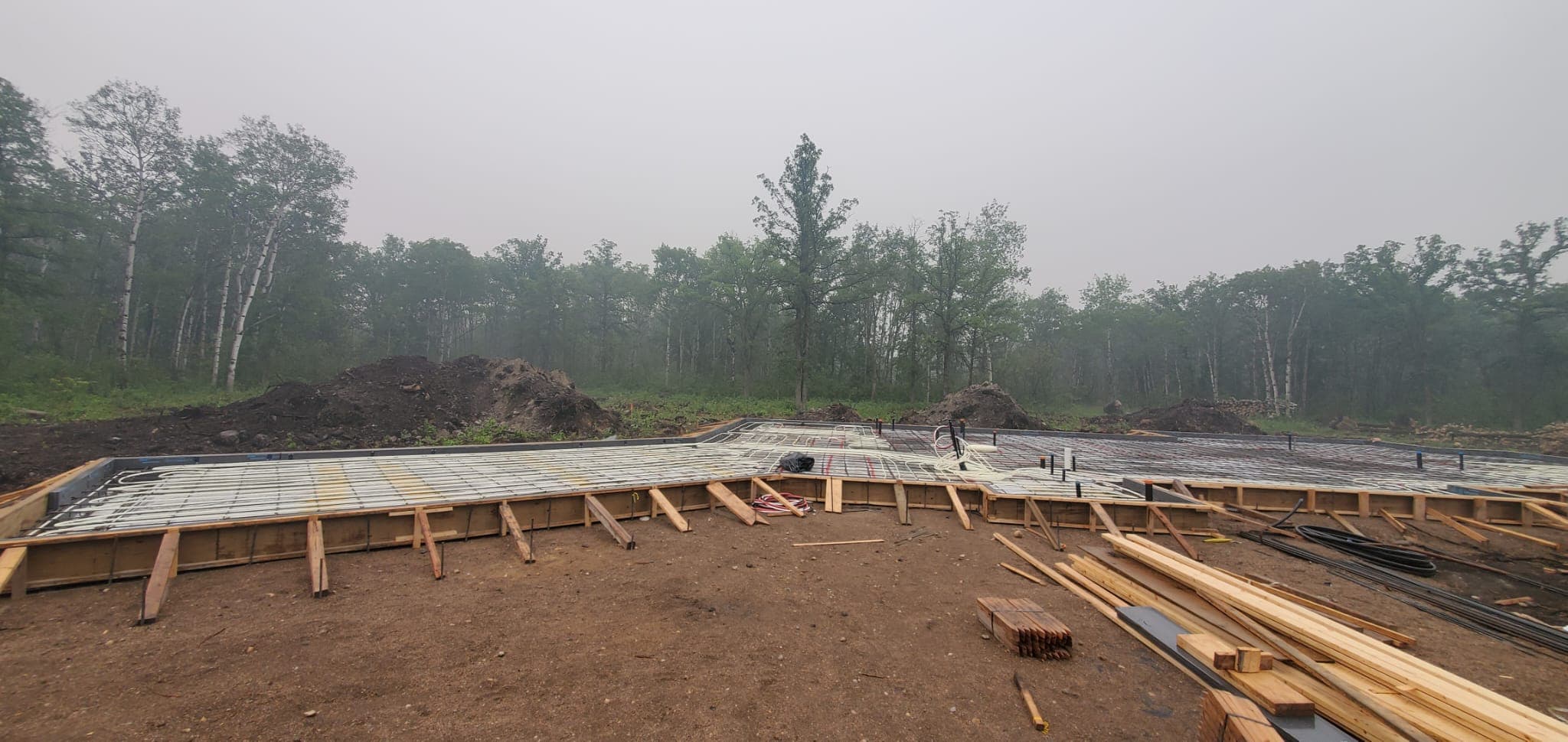 Radiant floor heating tubes installed in wooden foundation forms at a wooded construction site.