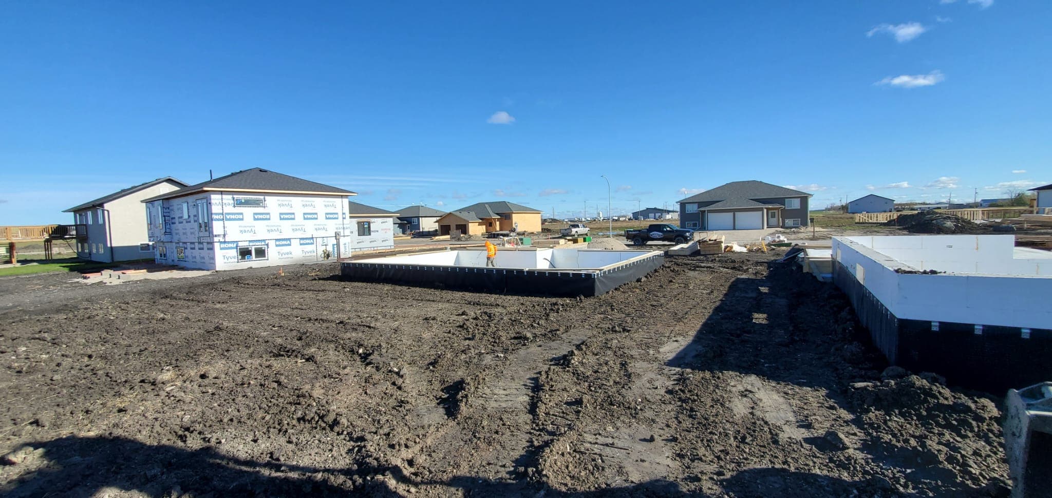 New residential construction site with concrete foundations and a partially built house on muddy ground.